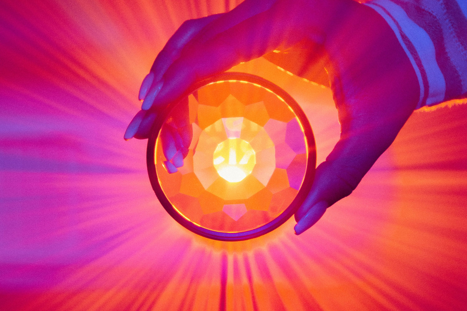 Hand holding circular glass emitting orange and pink colored lieght